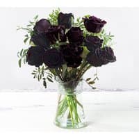Bouquet of black roses with green leaves in a clear glass vase.
