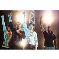 I don't know who these people are, but they are standing on stage with spotlights, wearing casual clothing, and pointing upwards.