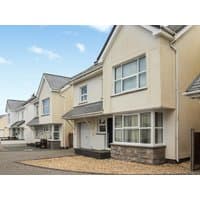 Beige two-story house with white trim, large front windows, and stone accents, part of a suburban row of similar homes.
