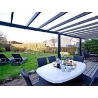 Outdoor patio set with white oval table, black chairs, under pergola, overlooking garden with loungers and hedges.