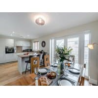 "Modern open-plan kitchen and dining area with light wood floors, white cabinets, and a table set for four with flowers."