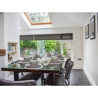 Dining area with glass table, six place settings, skylight, and garden view through large windows in a modern cottage.