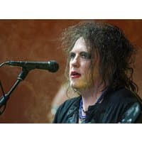 I don't know who this is, but it appears to be a person with curly hair and makeup standing at a microphone.