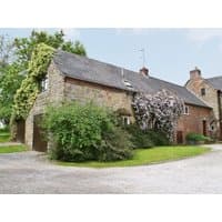 Stone and brick cottage with ivy, pitched roof, and lush garden, part of "The Garden House" by cottages.com.
