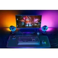 Black Razer Nommo V2 Pro speakers with cylindrical design, RGB lighting, and wireless connectivity on a gaming desk.