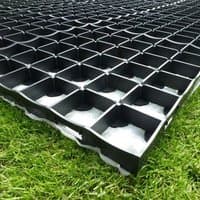 Black plastic grid-style shed base kit on grass, featuring interlocking square cells for stability.