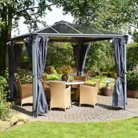 Palram Canopia gazebo with dark curtains, metal frame, and transparent roof, set in a garden with wicker furniture.