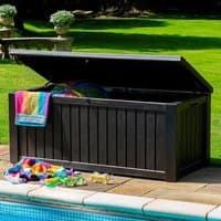 Brown Keter Rockwood plastic garden storage box with wood-like texture and hinged lid, placed poolside.