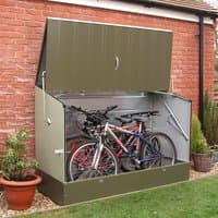 Green metal bicycle storage unit with lift-up lid, housing two bikes, against a brick wall.