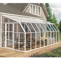 Clear sunroom with white frame, sloped roof, and glass panels attached to a house, featuring patio furniture inside.