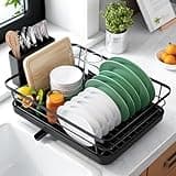 Black Kitsure dish drainer rack with cutlery holder, holding plates, bowls, and cutting boards on a kitchen counter.