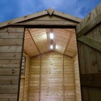 Solar lighting kit with two LED lights installed inside a wooden apex-roofed shed, door open, evening sky visible.