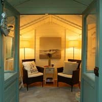 Solar lighting kit with two tall lamps, wicker chairs, and a central wooden table in a cozy garden building.