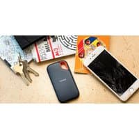Black SanDisk Extreme Portable SSD with rounded edges and orange loop, next to a cracked smartphone and keys.