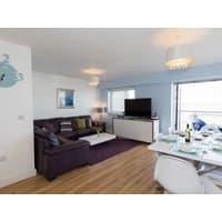 "Beach View" vacation rental living room with purple sofa, flat-screen TV, dining table set, and ocean-themed decor.