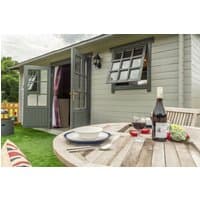 Wooden garden shed with open windows and doors, next to a patio table set with wine, glasses, and plates.