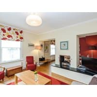 Cozy living room with red armchairs, floral curtains, wooden coffee table, and a flat-screen TV on a black stand.