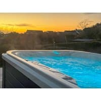 Outdoor hot tub with blue water and steam, set against a sunset backdrop and distant rooftops.