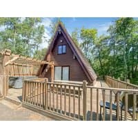 A-frame wooden cabin with large deck, surrounded by trees, featuring sliding glass doors and outdoor seating.