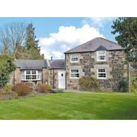 Stone Stable Cottage with two-story section, white framed windows, pitched roof, and lush green lawn.