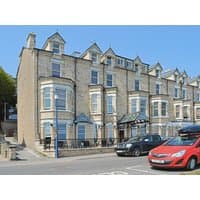 Stone terraced building with bay windows, blue trim, and pitched roofs, labeled "The Nest" by cottages.com.