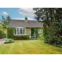 Stone cottage with ivy-covered walls, green door, large front windows, surrounded by trees and a grassy lawn.