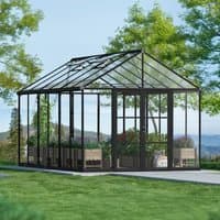 Black polycarbonate greenhouse with clear panels, gabled roof, and spacious interior, set in a lush garden setting.