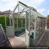 Modular wooden greenhouse, 10' x 8', with clear panels, green frame, and open door, set on a gravel path.