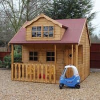 Wooden Swiss cottage playhouse with veranda, red roof, dormer window, and picket fence, set on gravel.