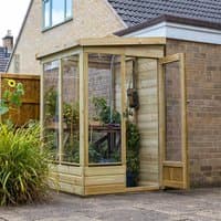 Wooden lean-to greenhouse with clear panels, solid back, and door, attached to a brick wall.