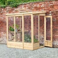 Wooden lean-to greenhouse with clear panels, open back, and door, set against a brick wall.