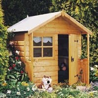 Wooden playhouse with pitched roof, front window, and open door, surrounded by greenery and flowers.