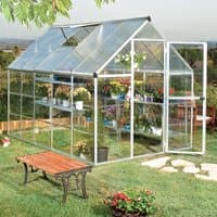 Silver polycarbonate greenhouse with clear panels, gabled roof, open door, and interior shelves, set in a garden.
