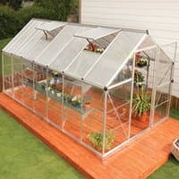Silver Palram Canopia greenhouse with polycarbonate panels, pitched roof, and sliding door on wooden platform.