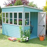 Teal wooden garden potting shed with six windows, open door, and gardening tools inside, surrounded by plants.