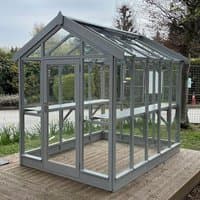 Greenhouse with gray-painted wooden frame, clear glass panels, pitched roof, and double doors on a wooden deck.