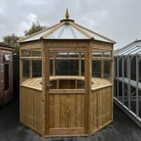 Octagonal wooden greenhouse with clear panels, pointed roof, and wooden door, measuring 7'10 x 7'10.