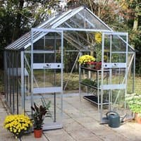 Greenhouse with toughened glass, silver aluminum frame, pitched roof, and sliding door, surrounded by plants.