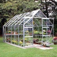 Green aluminum-framed greenhouse with clear glass panels, featuring plants and flowers inside, set on a grassy lawn.
