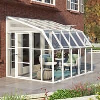 White Palram Canopia Rion sunroom with clear panels, sloped roof, and door, attached to a brick house.