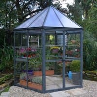 Hexagonal greenhouse with clear polycarbonate panels, gray aluminum frame, and a peaked roof.
