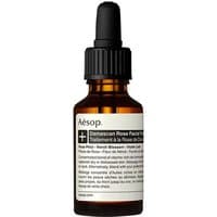 Amber glass bottle with black dropper cap, labeled "Aesop Damascan Rose Facial Treatment" for dry skin.