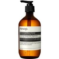Amber bottle with black pump, labeled "Aesop Geranium Leaf Body Cleanser 500 ml," minimalist design.