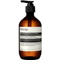 Amber bottle with black pump dispenser labeled "Aesop Reverence Aromatique Hand Wash 500 ml" in minimalist design.