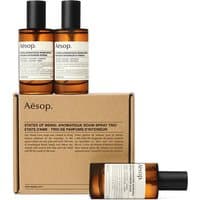 Amber glass bottles with black caps, labeled Aesop, atop a brown cardboard box labeled "States of Being Room Spray Trio."