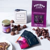 Assorted chocolate truffles, popcorn, and bars with packaging, including a jar of chocolate spread on a white surface.