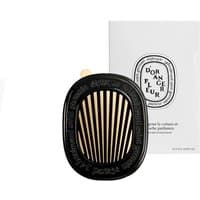 Diptyque Fleur d'Oranger car diffuser, black oval with gold slats, elegant floral design, white packaging in background.