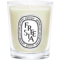 Clear glass Diptyque Freesia candle with white wax and black oval label featuring floral design.