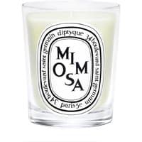 Clear glass jar with white wax, black Diptyque label featuring "Mimosa" text, floral scented candle.