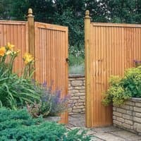 Wooden garden gate with vertical slats, natural finish, and decorative post caps, set in a lush garden setting.